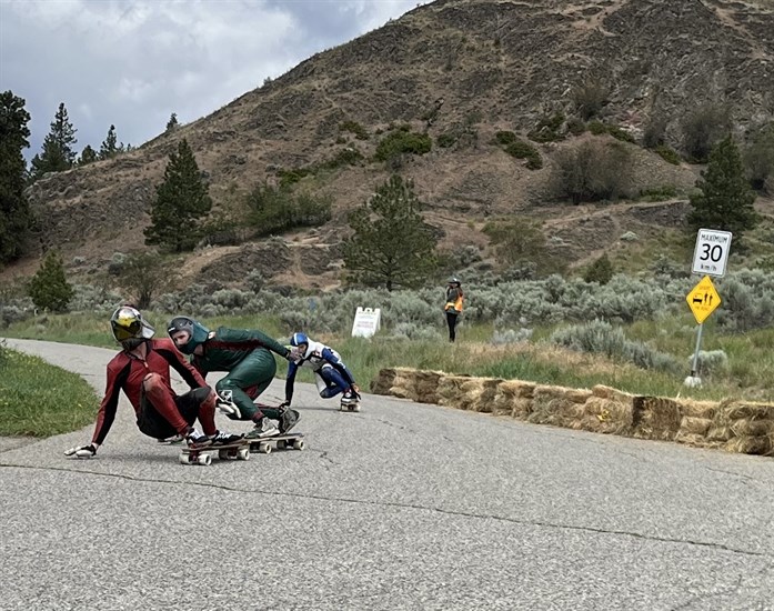 Three longboarders neck and neck at the hairpin turn on Knox Mountain Drive. 