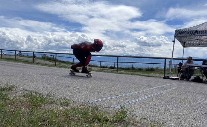 A longboarder in a tucked position for aerodynamic efficiency as they cross the finish line. 