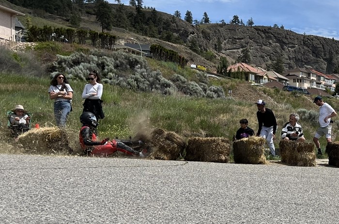 Spectators jump out of the way as a longboarder crashes into the row of safety hay bales.