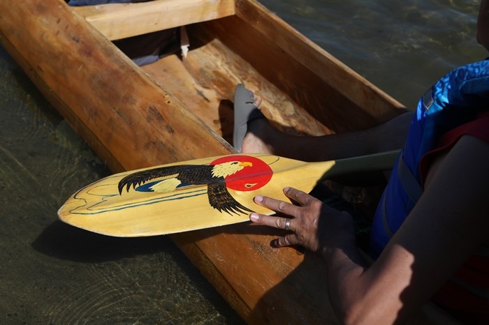 A community member readies their paddle during the launch of Herman Edward ties an eagle staff to a canoe, prior to the launch of the 2024 Suk?naqin canoe journey.