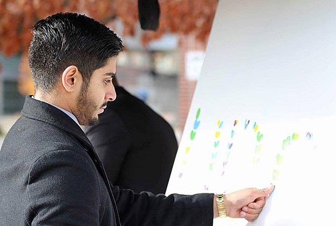 Event organizer and UBCO student Ryan Kaila adds his heart-shaped fingerprints to a poster at a moment of silence Wednesday.