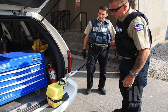 Penticton bylaw officer Glenn Duffield places a discarded needle in a sharps container while Darren Calibaba looks on in the background.